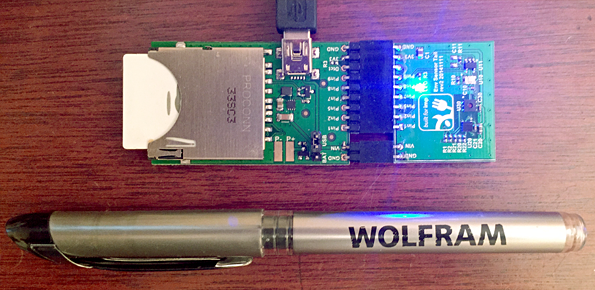 This device records the humidity, light, pressure, and temperature at my desk, and sends it to a Data Drop databin. The cable is power; the pen is there to show scale.