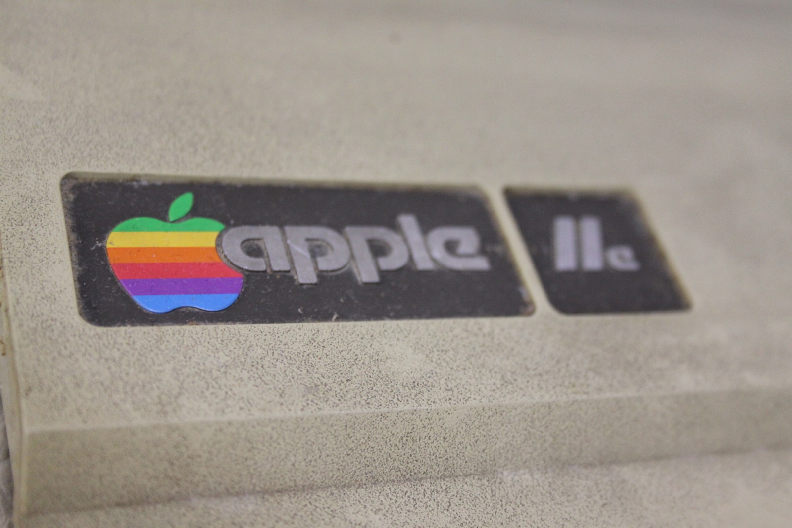 Фирменный значок Macintosh - цветное еще тогда яблочко. Модификация - Apple IIe. Отличается от оригинальной "двойки" кроме внешнего вида увеличенной оперативкой (Было 4/48КБ на выбор, стало 64 КБ), более дешевыми чипами ну и прочими не очень большими изменениями, для которых маркетологи решили не выпускать  новый Мак, а просто добавить буковку к названию)