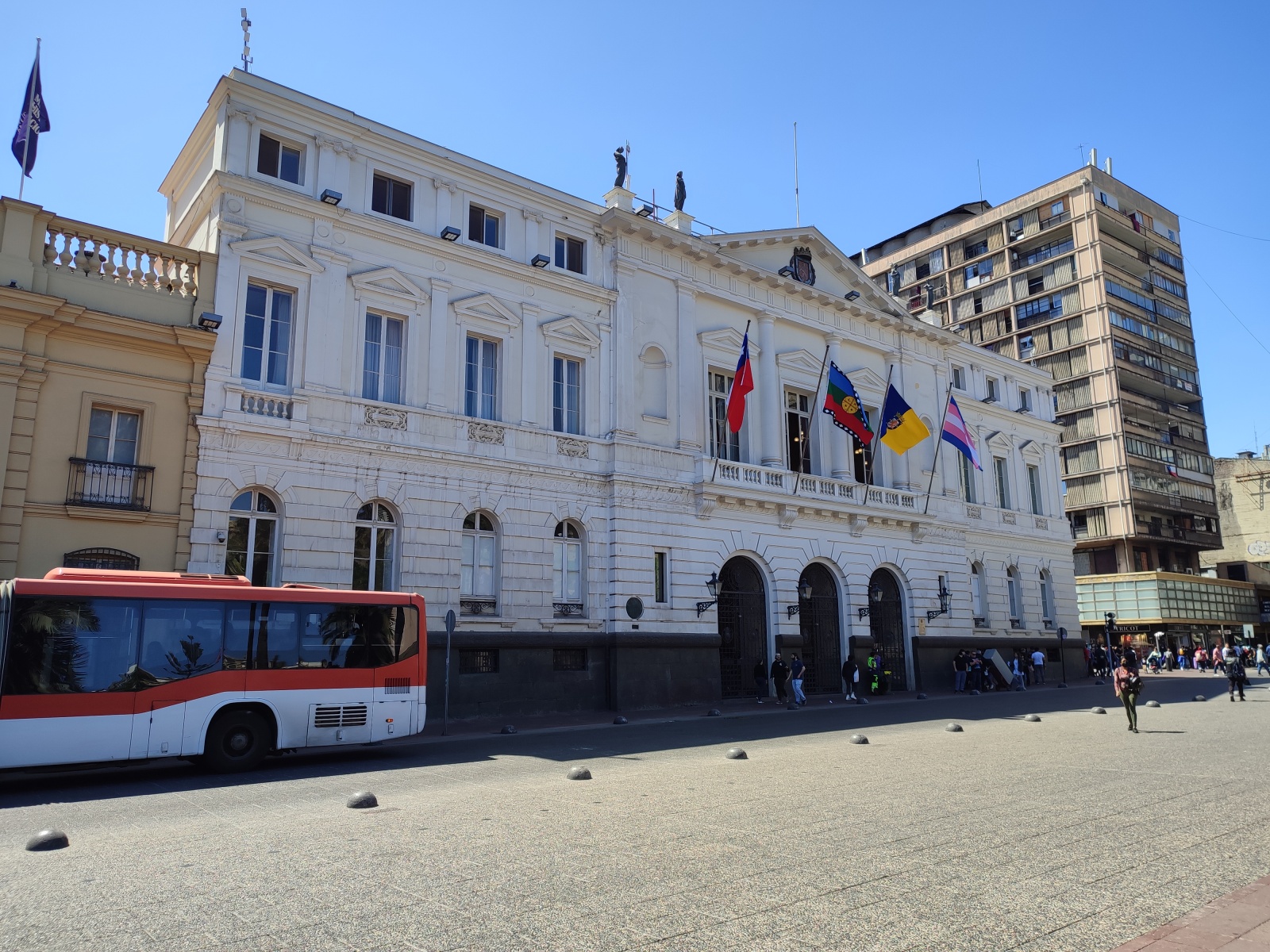 Здание муниципалитета Сантьяго на центральной площади. Слева направо: флаг Чили, флаг мапуче, флаг Сантьяго, флаг трансгендеров (обычно вместо него висит флаг ЛГБТ)
