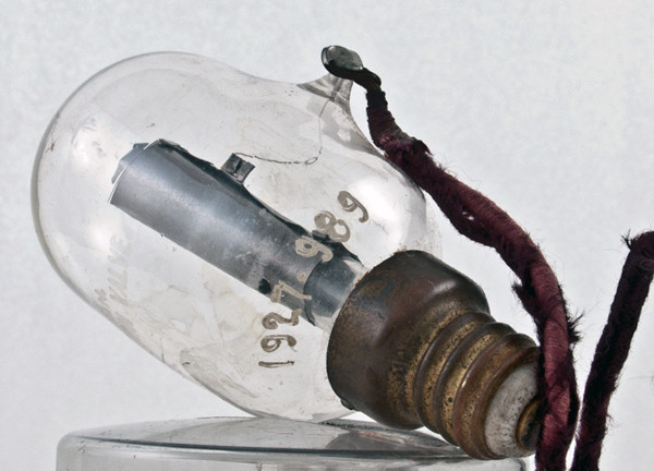 Фото 1.4. Первый вариант коммерческого «колебательного клапана» Флеминга для связи, с характерным ламповым винтовым цоколем. Выпущен британской фабрикой Edison and Swan, производившей осветительные лампы накаливания. Конструкция с традиционной гребешковой ножкой, на которой внутри баллона и установлен анод. Чтобы анод не ёрзал вверх-вниз, внизу металлического цилиндра пробито отверстие, которым он (анод) насажен на специальную стеклянную пупочку на ножке лампы. Вывод анода выполнен платиновой нитью, впаянной в стенку колбы. Снаружи к нему мягким припоем припаян гибкий медный провод в шёлковой изоляции