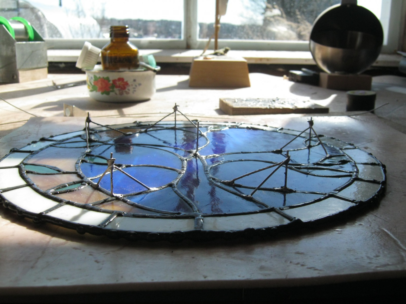 Фото 2.2. Более или менее равномерно распределяем по площади светильника стойки, обезжириваем и зачищаем на швах места для них, впаиваем. Стойки удобно выполнять из медного лужёного провода, например, старого обмоточного с зачищенной лаковой изоляцией, диаметром около 1 мм. Паяльник электрический, мощностью 80…150 Вт, с регулированием температуры жала. Хорошо работает простой диммер для ламп накаливания, тем более что существуют их варианты, встроенные в розетку. Флюс спиртоканифольный. Выравниваем высоту стоек, приложив к ним шаблон и обрезав лишнее бокорезами. Большая высота стоек позволяет подсветке быть более равномерной и рассеянной, но открытые сбоку светодиоды становятся видны лучше. Оптимальная высота — 2…2.5 см. Укрепляем стойки несколькими раскосами, впаянными в подходящие места швов, удаляем остатки флюса, восстанавливаем защитно-декоративное покрытие швов витража, обрабатываем и новые элементы, за исключением кончиков стоек