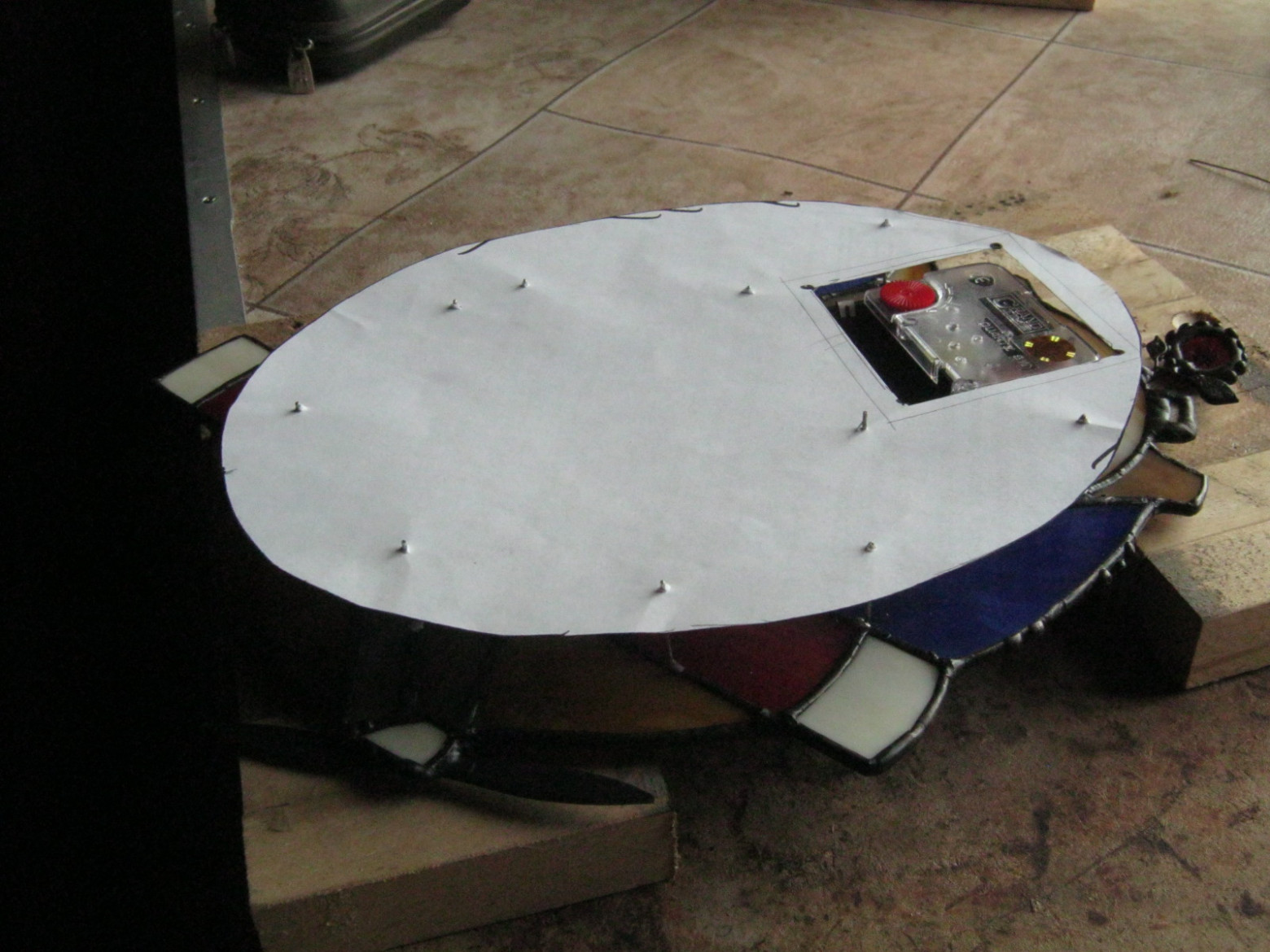 Фото 2.4. Перенесём точное положение стоек на пластину лампы при помощи промежуточного шаблона: приложим заготовку к листу нетолстой бумаги, очертим контур, вырежем ножницами. Приложив бумажный шаблон к витражу со стойками, наколем их концами отверстия, накерним и просверлим их на металле