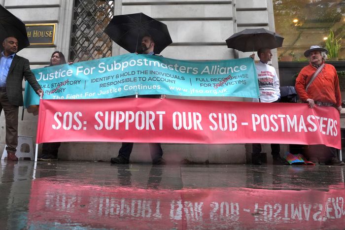 A crowd of protestors on a rainy day hold signs showing support for the Sub-postmasters.