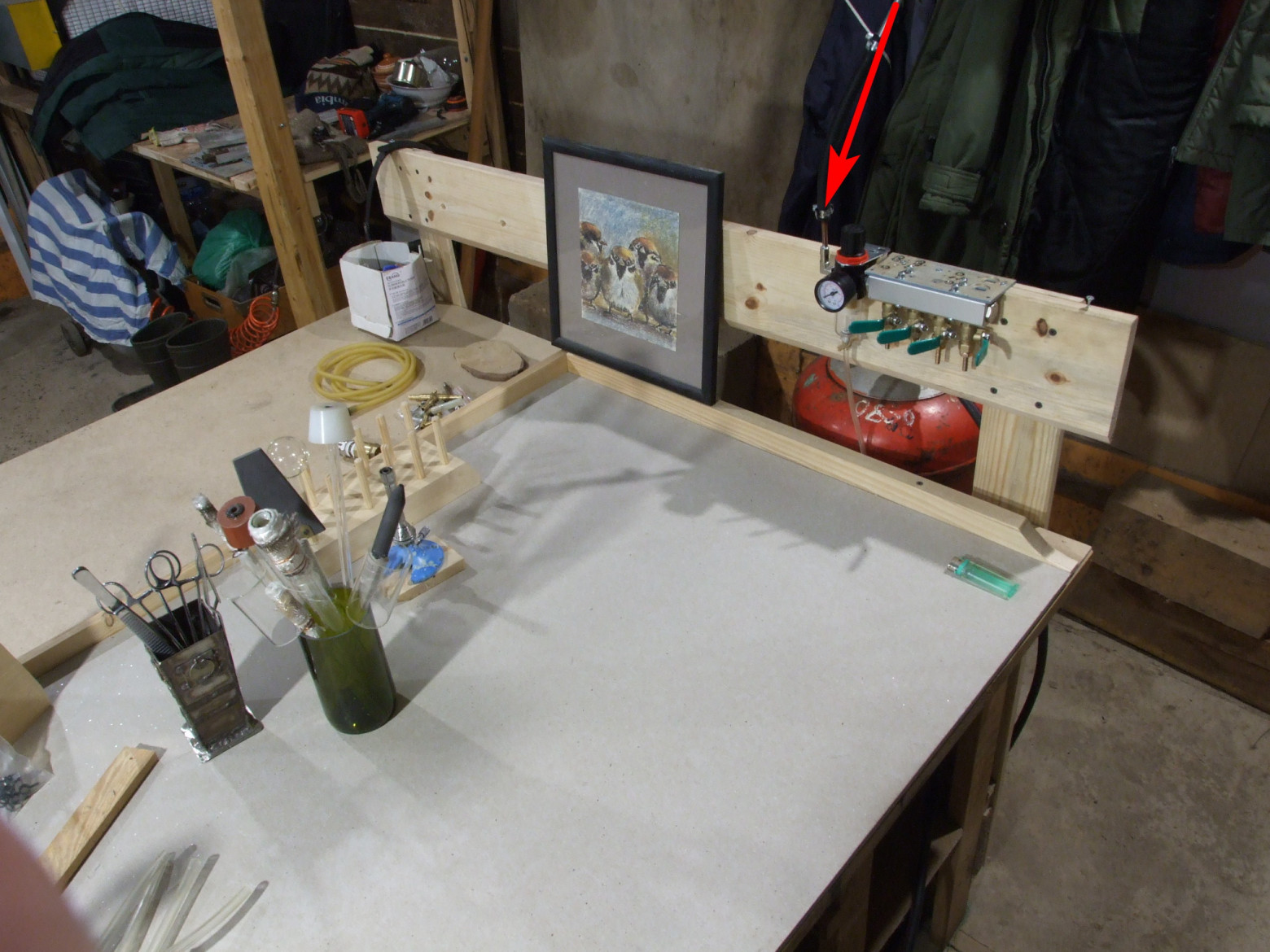 Фото 3.1. Для размещения газовых коллекторов-гребёнок, на одном из краёв рабочего стола предусмотрена специальная доска. За ней оставлено немного места для местного размещения газовых баллонов. На фото — смонтированный пневматический коллектор, стрелочкой отмечена воздушная магистраль, проложенная по потолку к компрессору