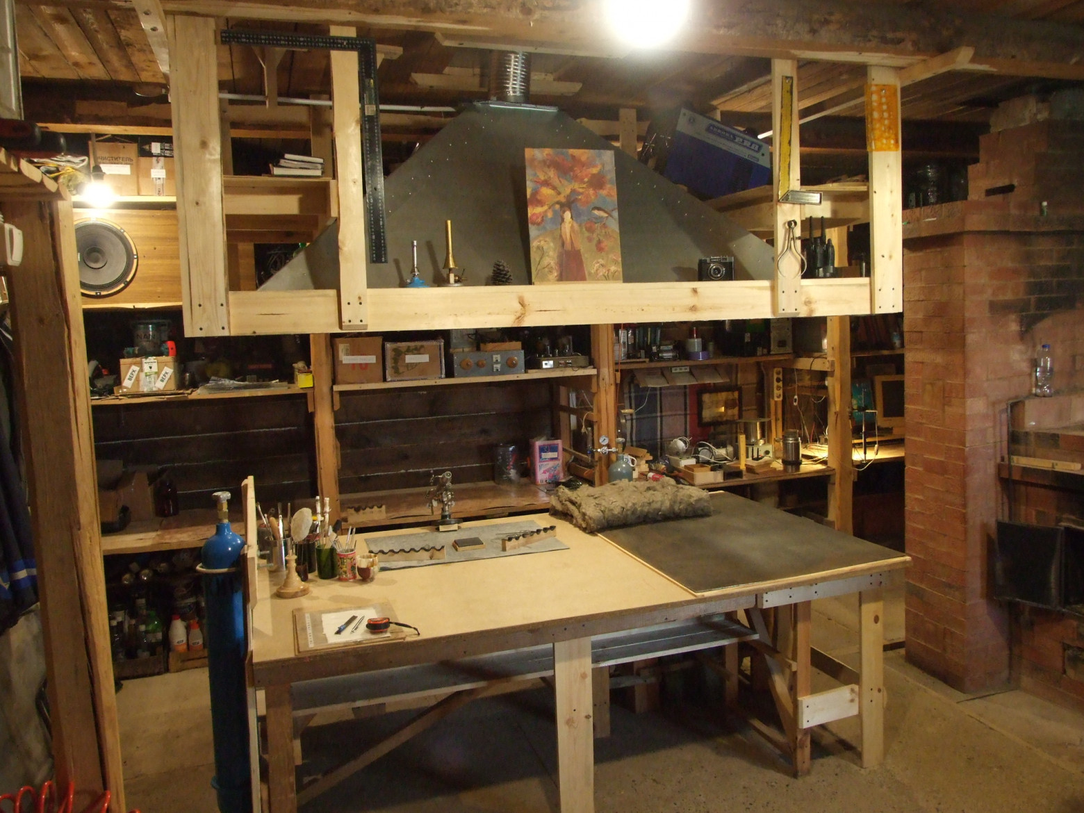 Фото 1.2. В дальнем от окна углу мастерской [4] собрал большой отдельно стоящий стол-остров и крупный вытяжной зонт над ним. Теперь можно позволить себе огни и заготовки несколько крупнее, есть место для баллонов внутри и за стеной, работу мастера (книксен) удобно фотографировать со всех сторон