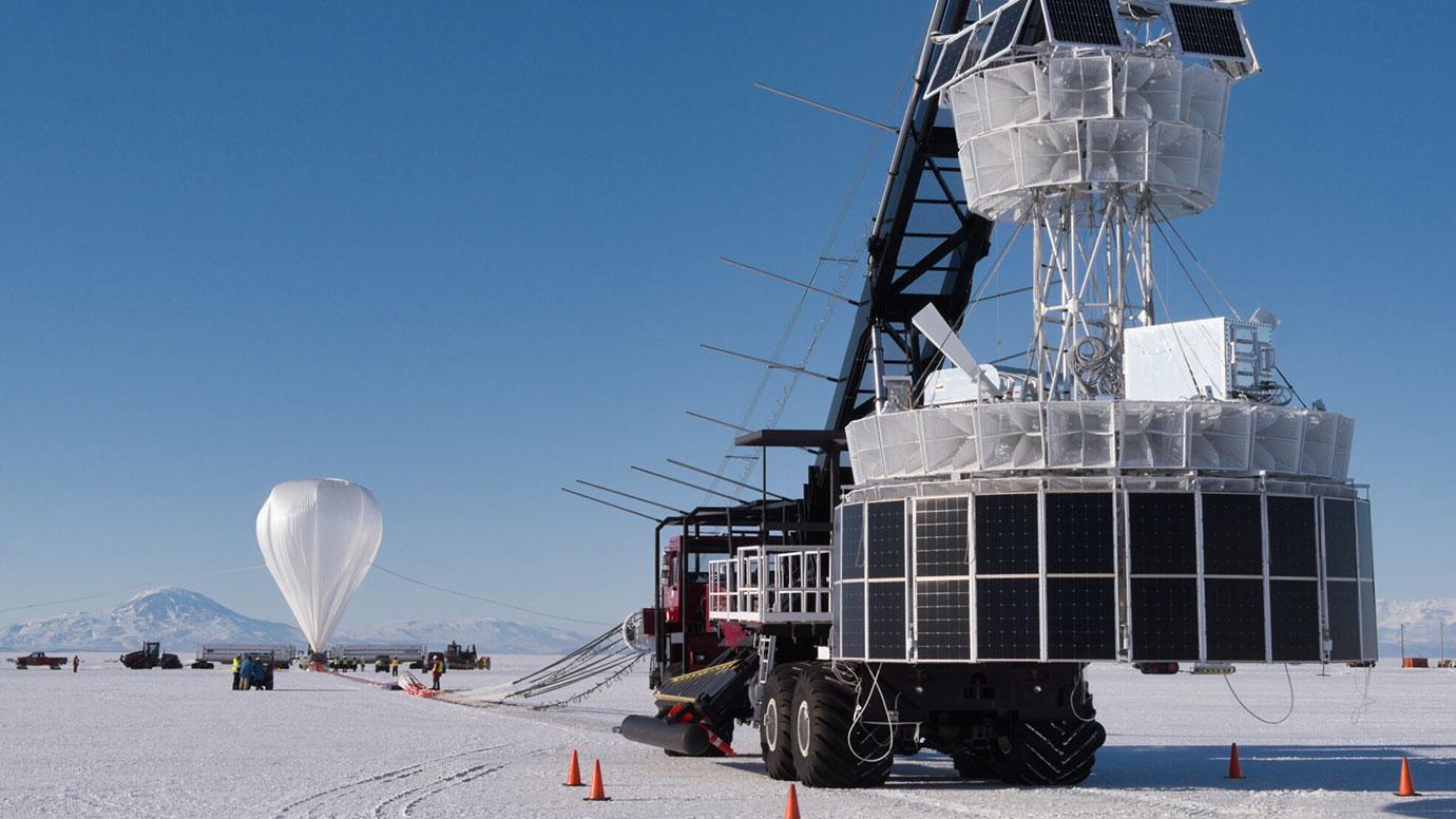 Пусковой автомобиль с PUEO (справа, покрытый антеннами и солнечными панелями) на стартовой площадке для миссии под руководством Чикагского университета. Воздушный шар НАСА (слева) в течение многих недель носил его вокруг Южного полюса
