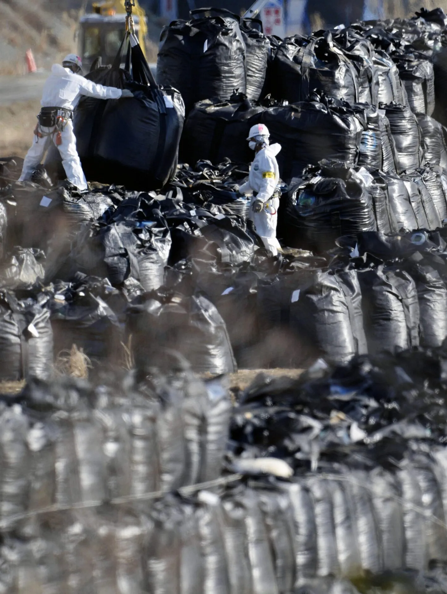 Workers pile hundreds of bags containing waste from soil decontamination work in Okuma, Fukushima Prefecture, in January 2014, three years after the March 11, 2011, earthquake and tsunami that triggered the nuclear crisis at the Fukushima power plant. <span class="feature_caption_credit">Kyodo News Stills via Getty Images</span>