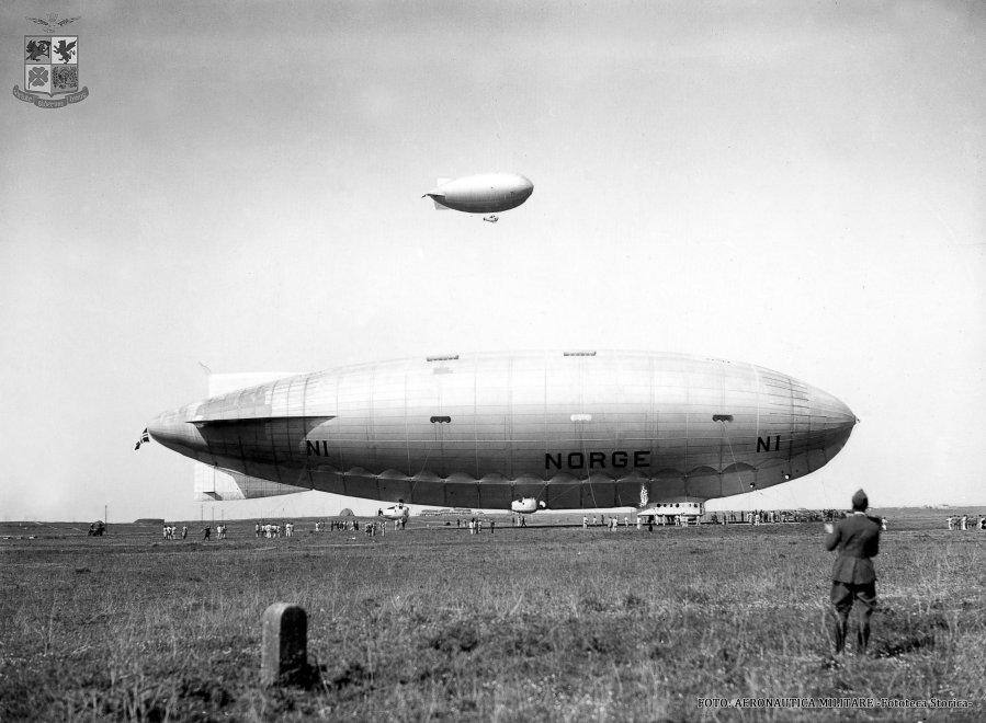 «Норвегия» перед отправкой в путь, аэродром Чампино близ Рима. На заднем фоне пролетает один из небольших дирижаблей мягкой конструкции из состава итальянского королевского флота: дешёвые и простые «блимпы» продолжали активно использовать в разных странах мира