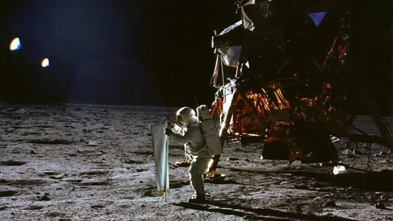 В 1969 году миссия «Аполлон-11» впервые доставила людей на поверхность Луны. На снимке изображён Базз Олдрин, устанавливающий экспериментальную установку «Солнечный ветер» в рамках миссии «Аполлон-11», а Нил Армстронг делает фотографию.