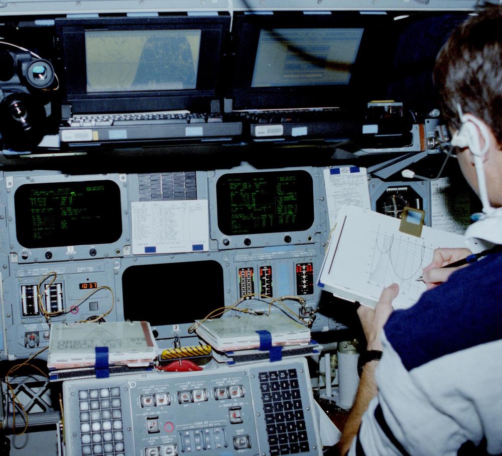 Three of the Shuttle's CRT displays. (Click for a larger image.) The left screen shows the Universal Pointing attitude display. The right screen shows the Relative Navigation screen for rendezvous operations. At the bottom of the photo are the two grid-style keyboards for communication with the computer, with the CRT controls in between. Two laptops are sitting on top of the console. Mission Pilot Kevin Chilton is in the pilot's seat. From National Archives.