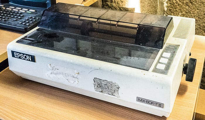 Photograph of a somewhat dirty and sticker-encrusted dot matrix printer.