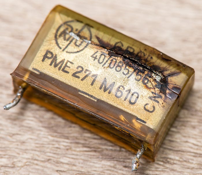 Close-up photograph of a capacitor with a clear split in the casing and scorch marks.