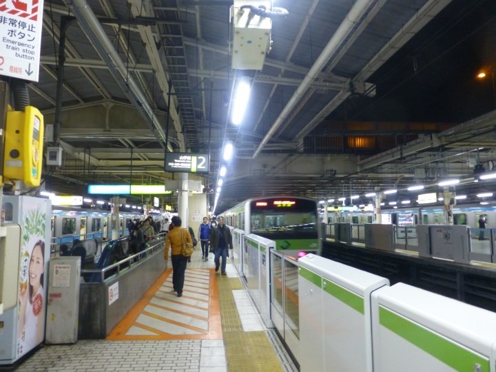Nighttime view along a Tokyo station platform, a green-striped Yamanote train behind white platform-edge doors.